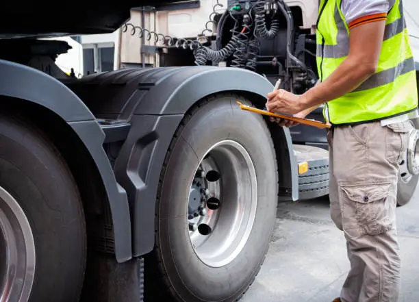 Technician inspecting a large truck tire with a pressure gauge.