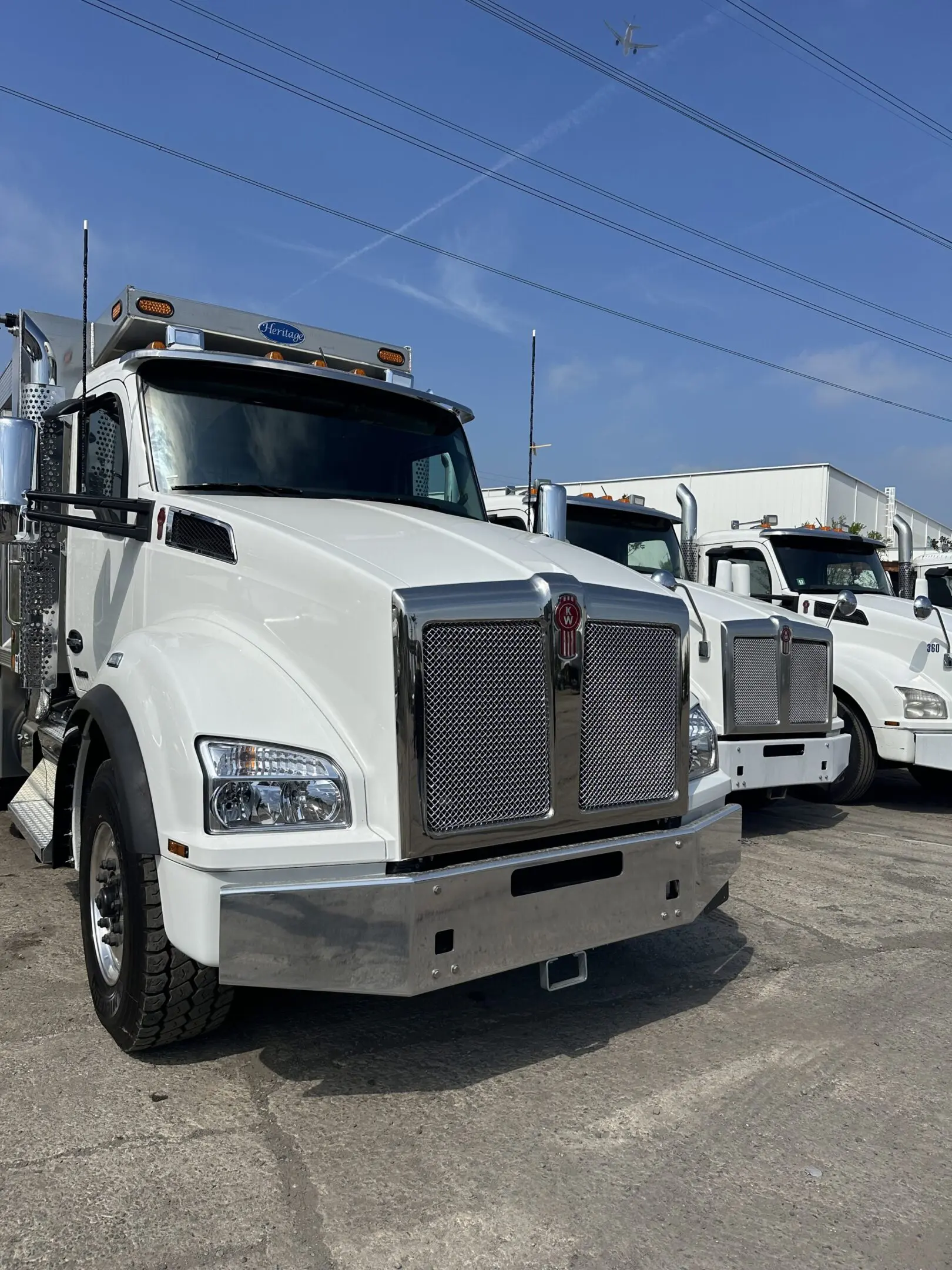 Two white semi trucks parked side by side under a clear blue sky.