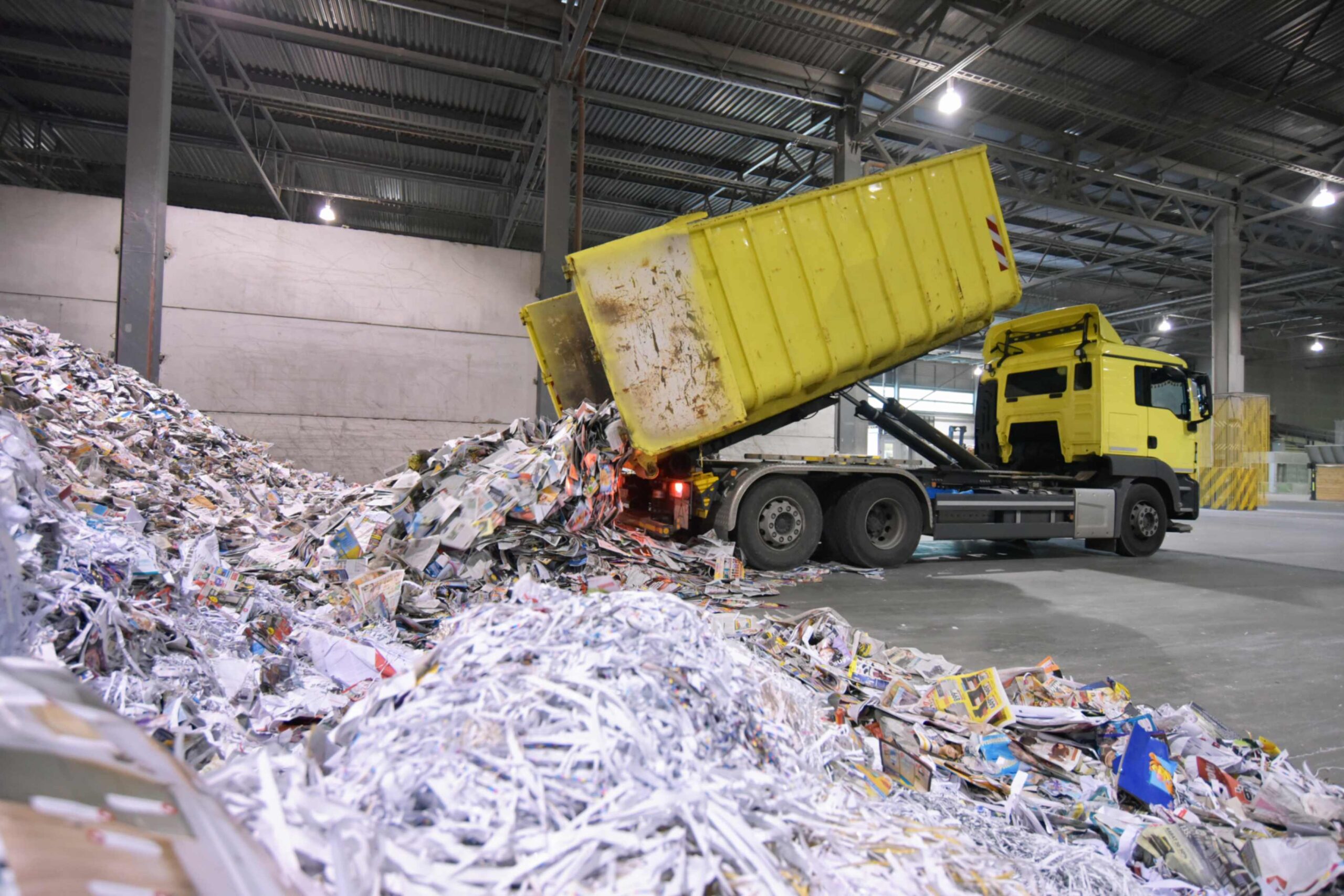 A yellow truck unloading shredded paper inside a warehouse.